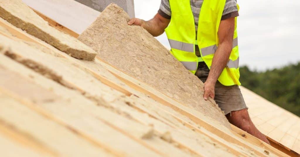 Homme portant une chasuble de chantier en train d'isoler une toiture par l'extérieur