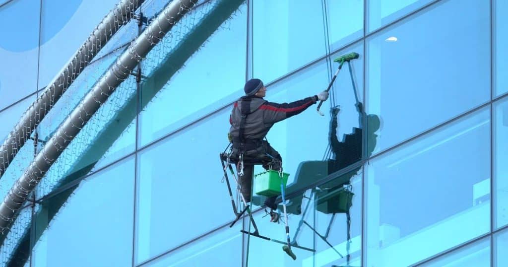 Laveur de vitre professionnel en train de laver les surfaces vitrées d'un immeuble à l'aide d'un cordage