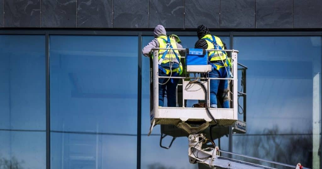 deux ouvriers en train de nettoyer les vitres d'un immeuble depuis une nacelle de chantier
