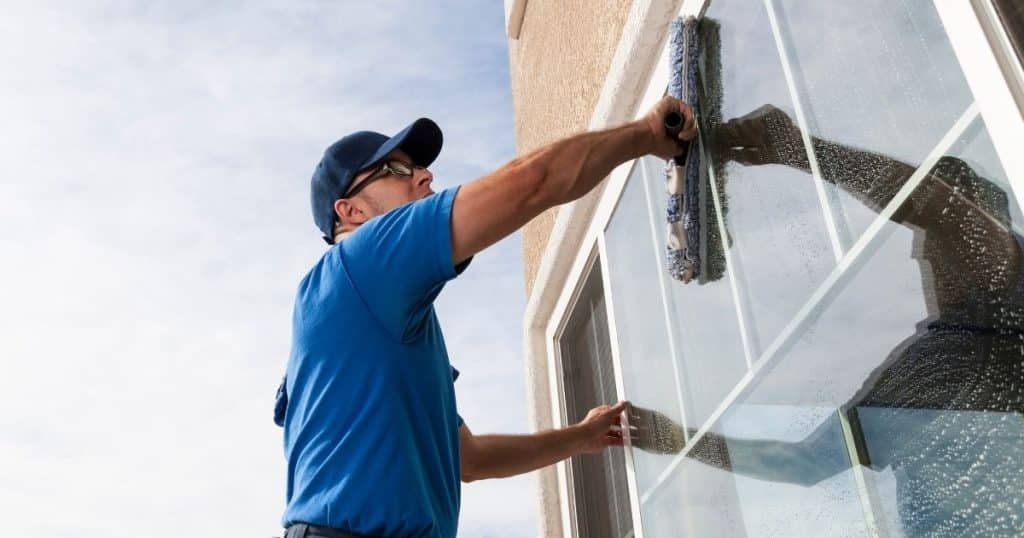 laveur de vitre professionnel en train de nettoyer les vitres d'une maison à l'aide d'une brosse