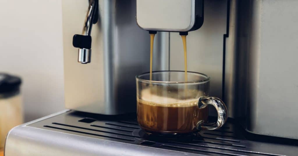 machine a cafe espresso en état de marche avec du café qui coule dans une tasse en verre dans un bureau