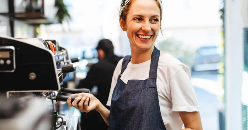 serveuse souriante en train de faire un café pour un client de son restaurant à l'aide d'une machine barista professionnelle pour horeca