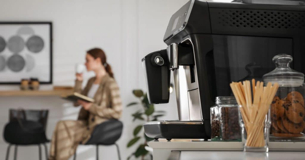 machine à café professionnel à l'avant plan et travailleuse en train de déguster un café dans l'espace café dédié de son entreprise