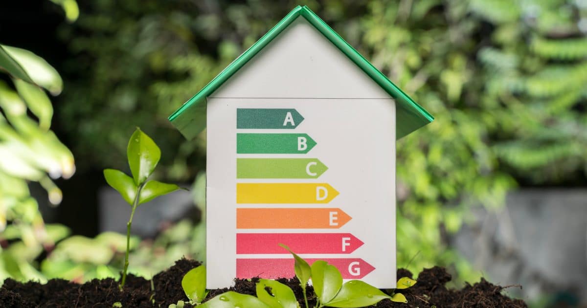 Un modèle de maison avec des niveaux d'efficacité énergétique de A à G placé sur le sol avec des plantes vertes, symbolisant la conception de la maison écologique, la vie durable, la responsabilité environnementale et l'utilisation efficace de l'énergie.