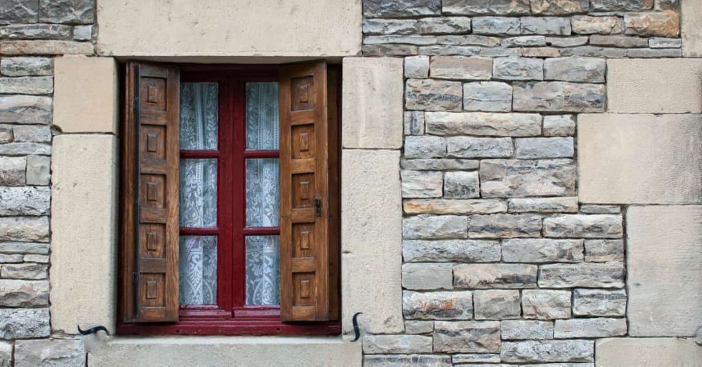 Mur en pierre d'une habitation avec une fenêtre et des volets en bois