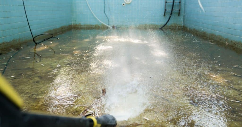 Personne qui nettoie une piscine complètement vide à l'aide d'un tuyau d'arrosage. 