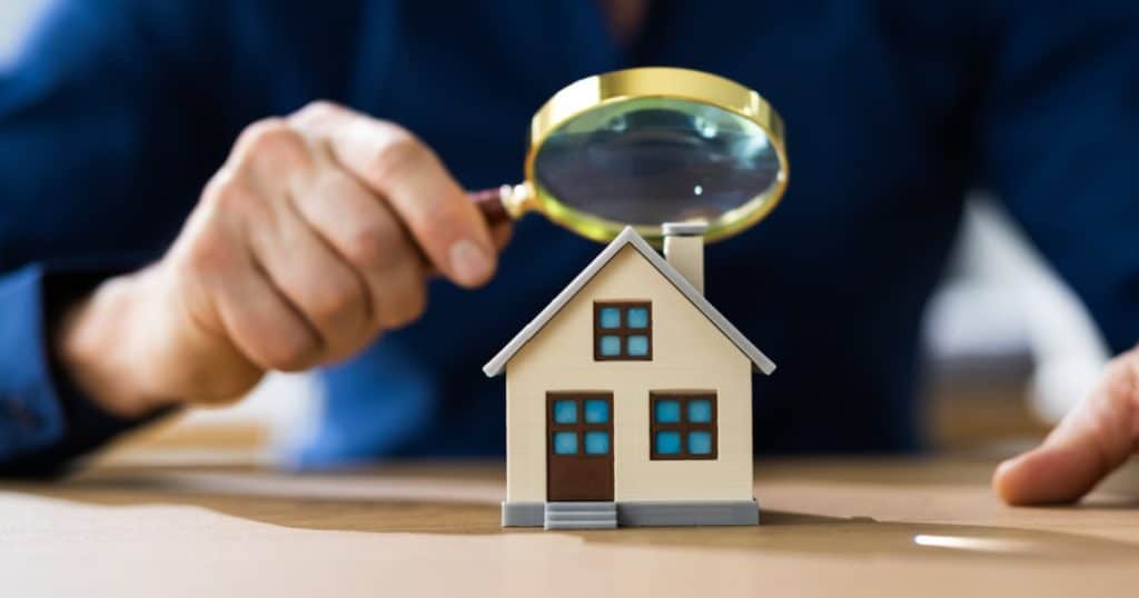 Un homme regarde avec une loupe la maquette miniature d'une maison. 