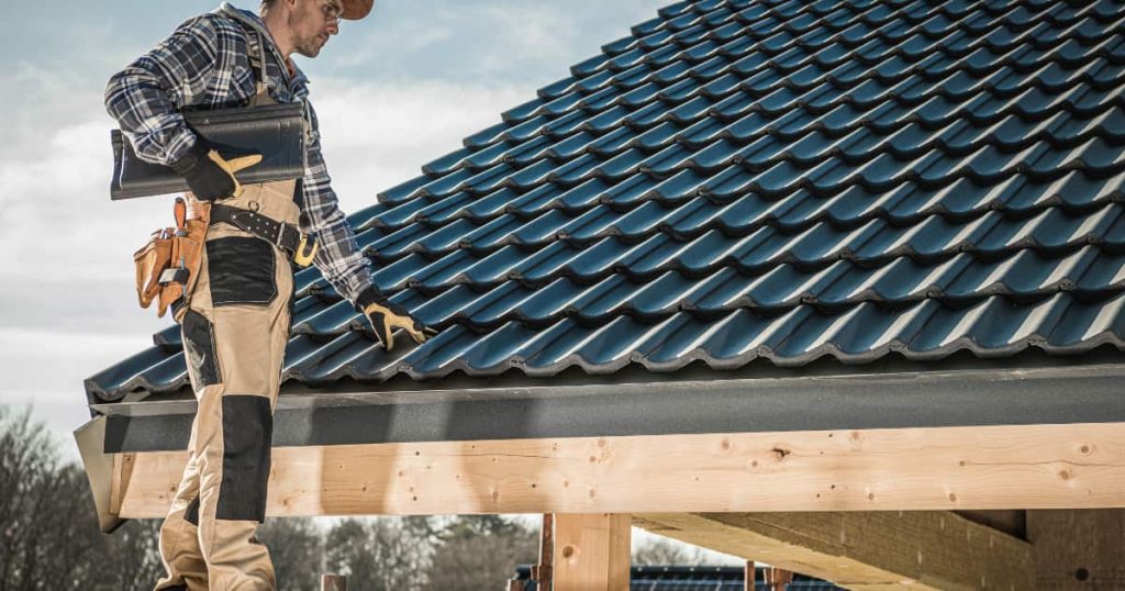 Couvreur posant des tuiles noires sur un toit neuf en bois