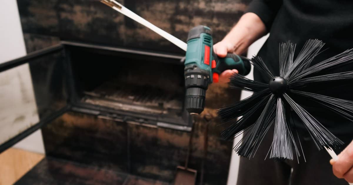Un homme devant une cheminée tenant un kit de nettoyage à base de suie et une perceuse. Entretien de la maison, service du système de chauffage et préparation pour la saison d'hiver.