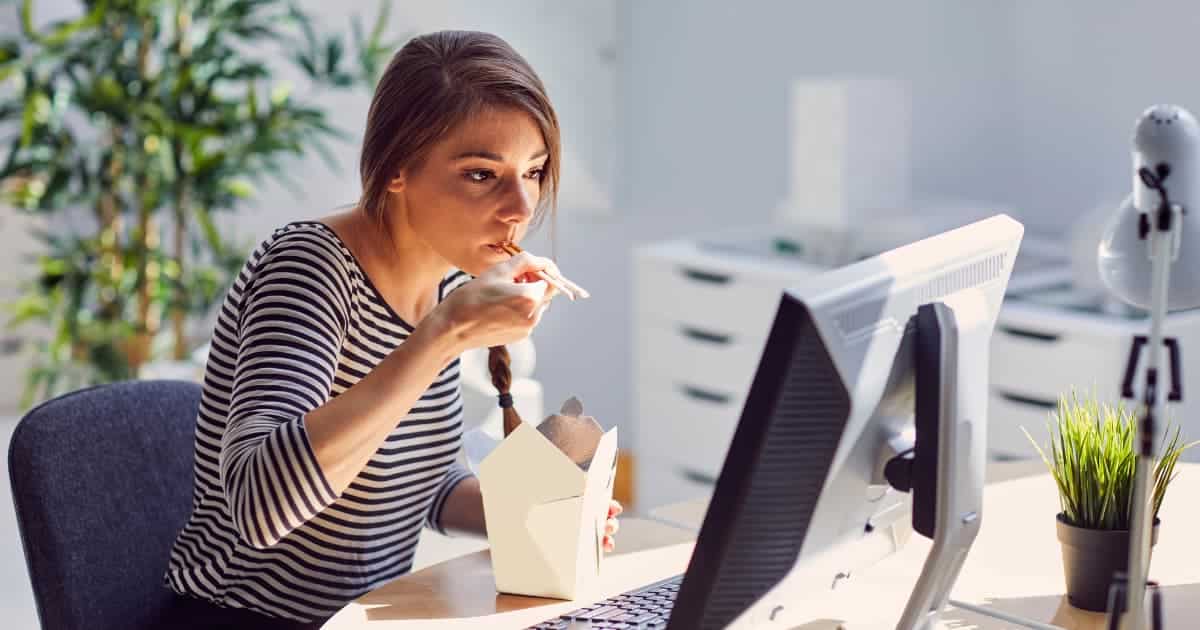 Une femme assise dans son bureau et mange des nouilles devant son ordinateur