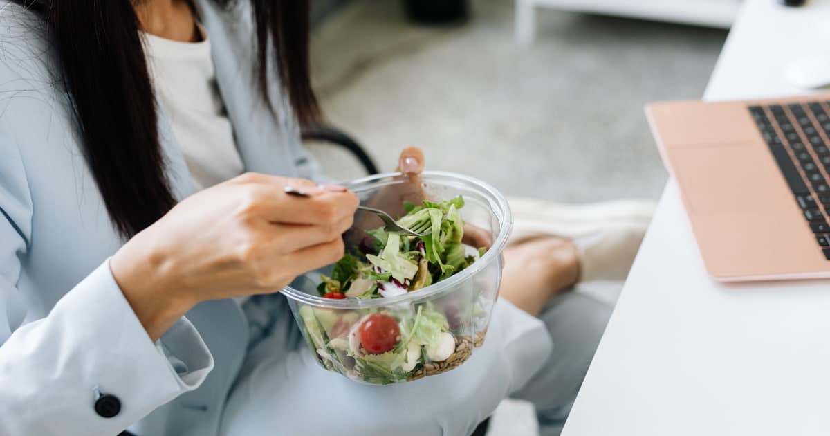 Femme mangeant une salade devant son ordinateur portable au bureau.
