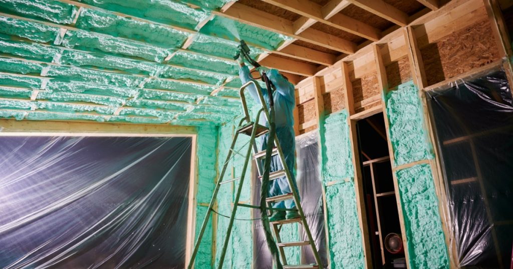 Personne en combinaison qui isole le plafond d'une pièce à l'aide de mousse de PUR projetée de couleur verte 