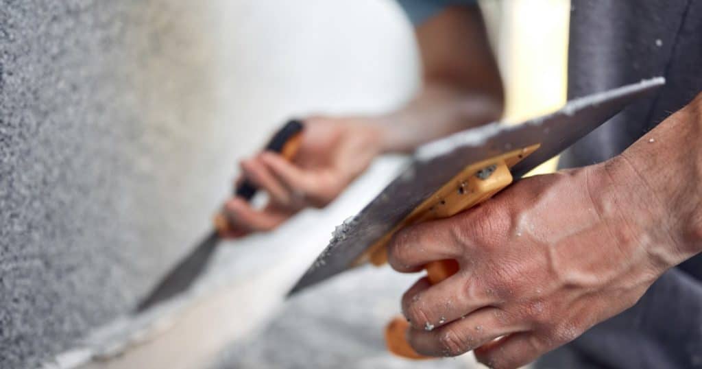 Un homme pose un crépi sur un mur extérieur avec des spatules et truelles. 