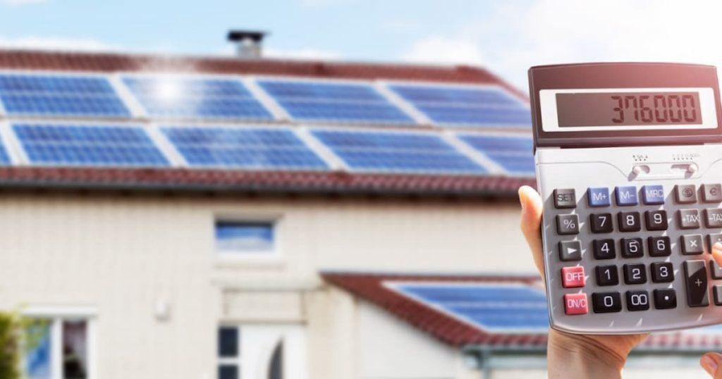 calculatrice affichant un haut montant devant une maison avec panneaux solaires