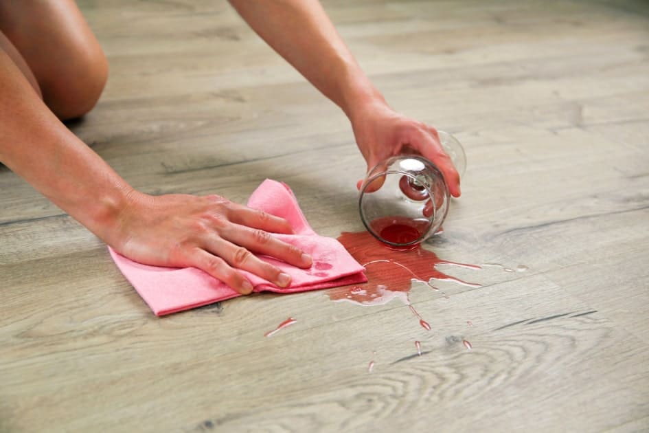 Une personne éponge le vin d'un verre renversé sur du parquet avec une lingette microfibre. 