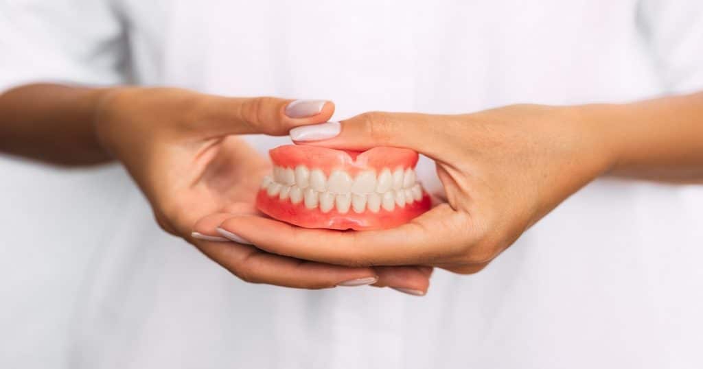 Une dentiste tient un dentier entre ses mains. 