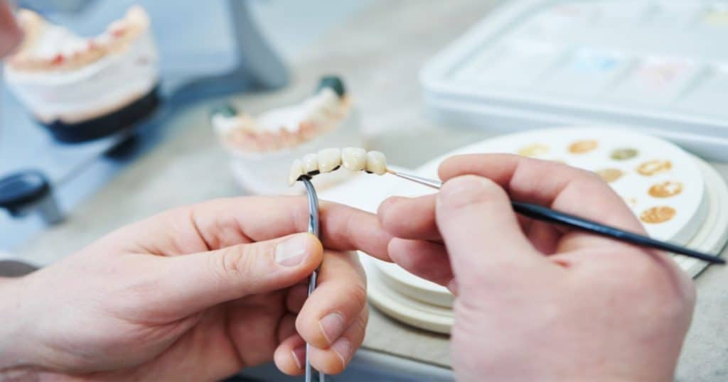 Un dentiste retouche la prothèse dentaire d'un patient dans son laboratoire. 