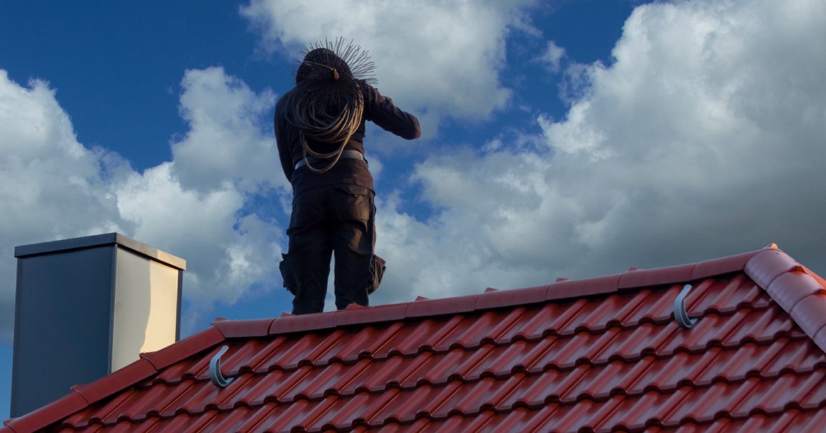 Ramoneur sur le toit d'une habitation avec ses outils de travail.