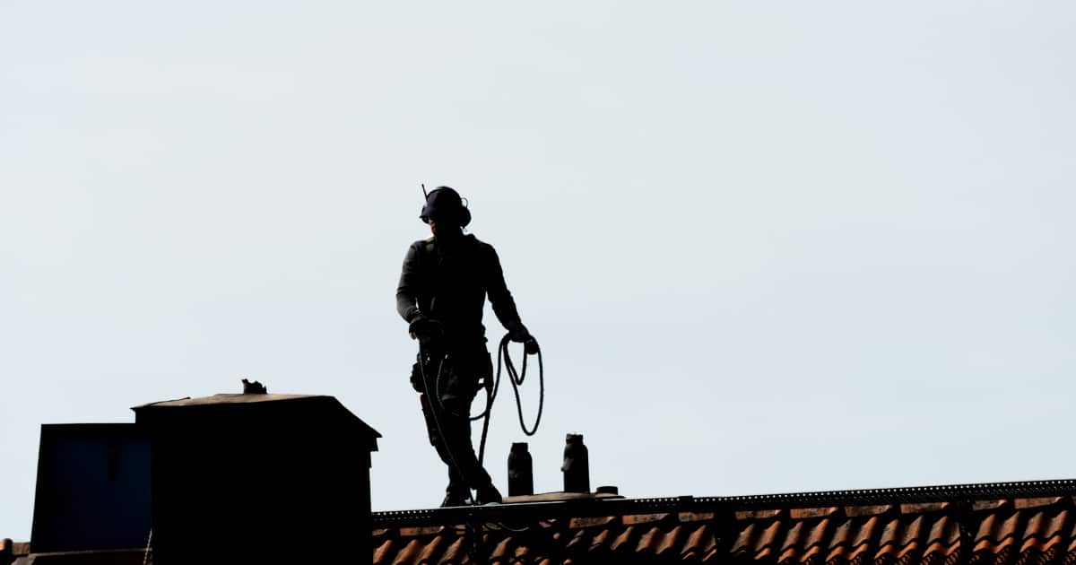 Un ramoneur sur le toit d'une maison pour s'occuper d'une cheminée.