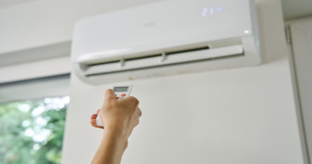 Réglage de la température du climatiseur avec télécommande. La main tient la télécommande et met la température confortable sur le système climatique dans l'appartement