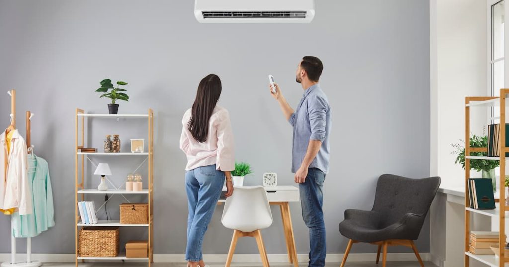 Le couple familial met le système de climatisation à la maison. Jeune mari et femme debout dans le salon, regardant l'unité AC blanche sur un mur gris, utilisant la télécommande et changeant la température à la maison