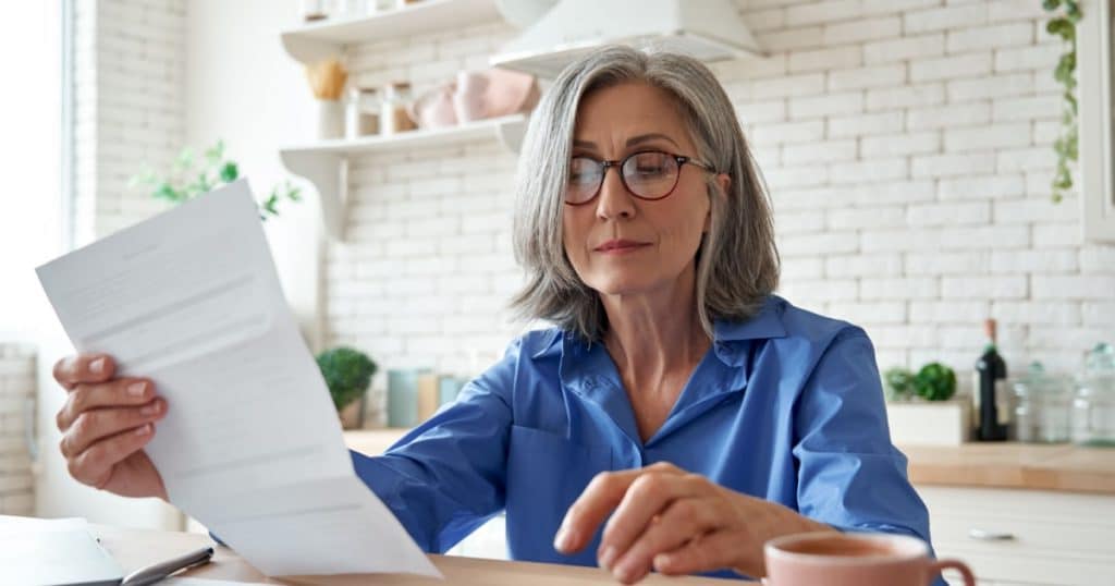 Une femme portant des lunettes est attablée avec un café et regarde une facture papier.