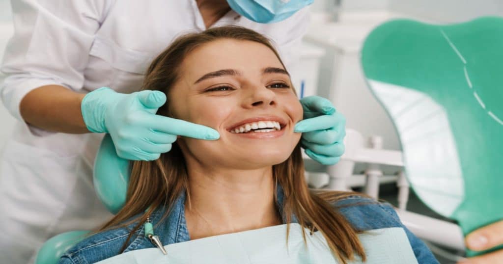 Une jeune femme souriante s'apprête à se faire examiner les dents par un dentiste. 