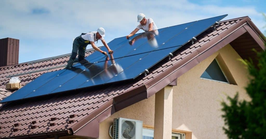 Deux ouvriers installent des panneaux solaires sur la toiture d'une maison. 