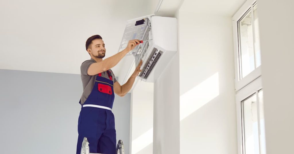 Travailleur masculin réparant l'air conditionné à la maison. Homme en uniforme debout sur l'échelle et installant un nouvel air conditionné sur un mur blanc dans la maison. Installation, entretien et réparation des CA
