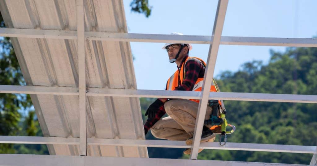 Un ouvrier se tient sur la structure d'une véranda pour changer le toit. 