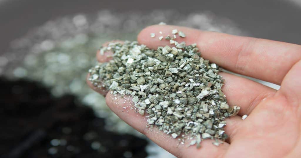 Vermiculite en granulés dans une main à l'avant-plan et un tas de vermiculite en granulés flouté en arrière-plan.