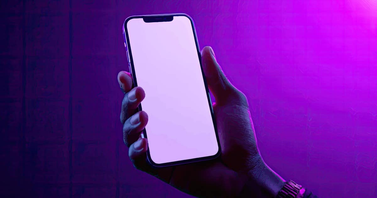 Smartphone tenu en main avec un mur violet en fond.