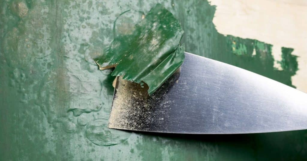Spatule qui racle une couche de peinture verte après un décapage