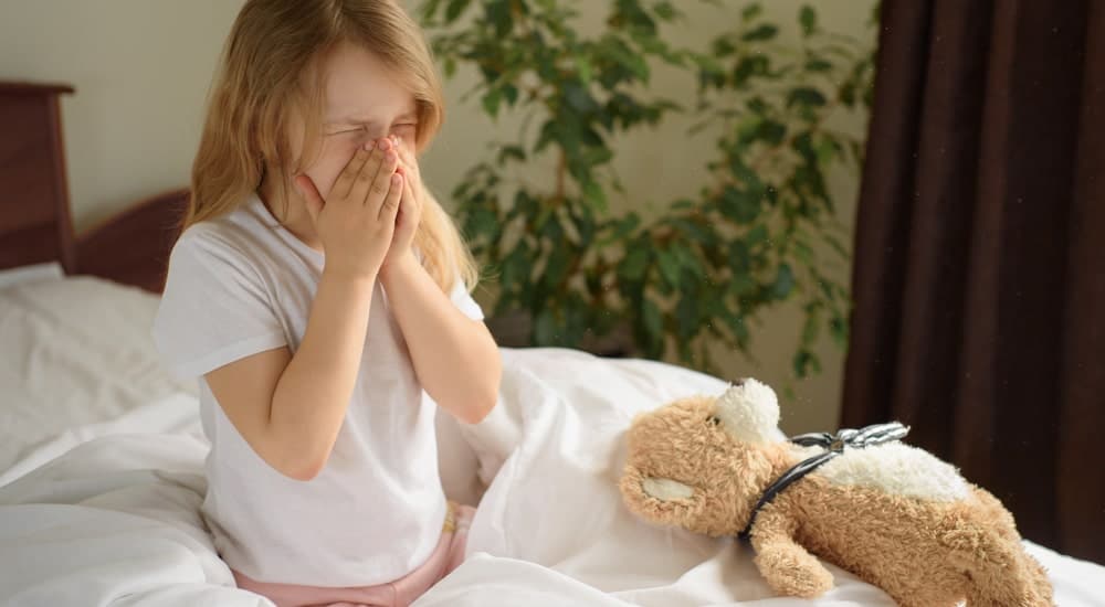 Une enfant avec sa peluche qui éternue dans son lit. 