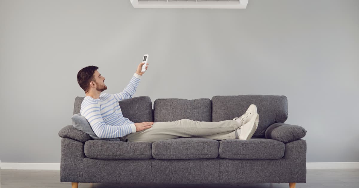 Homme allongé sur son sofa en train de régler la température de son climatiseur