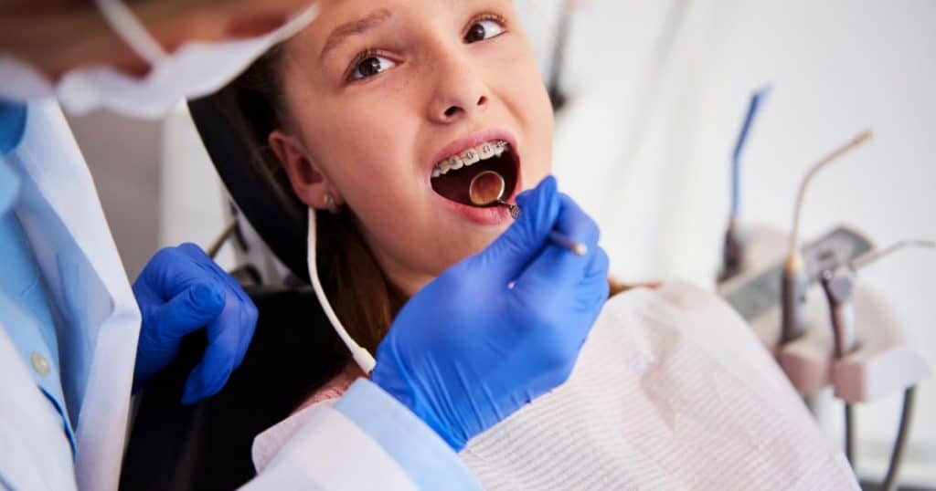 Un orthodontiste examine une adolescente qui porte un appareil dentaire.