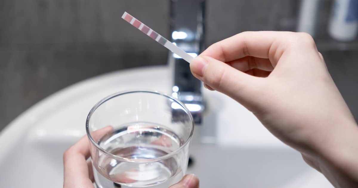 Gros plan sur une bandelette de contrôle de la qualité de l'eau sur un verre d'eau du robinet dans une salle de bain, essentielle pour vérifier la pureté, la santé et la filtration à domicile.