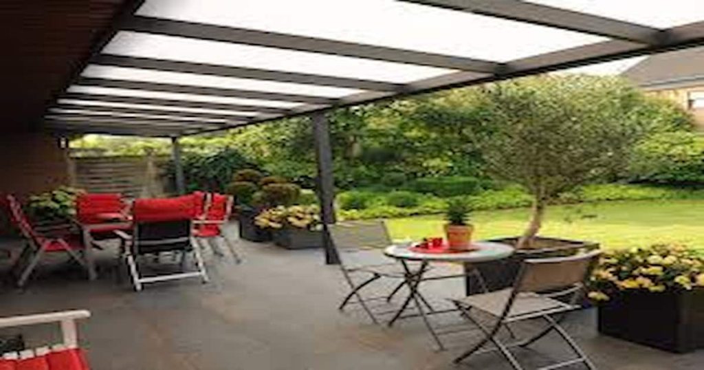 Terrasse avec table et chaises rouges et une vue sur un jardin avec pelouse ensoleillé et au-dessus couverture de terrasse en polycarbonate transparent