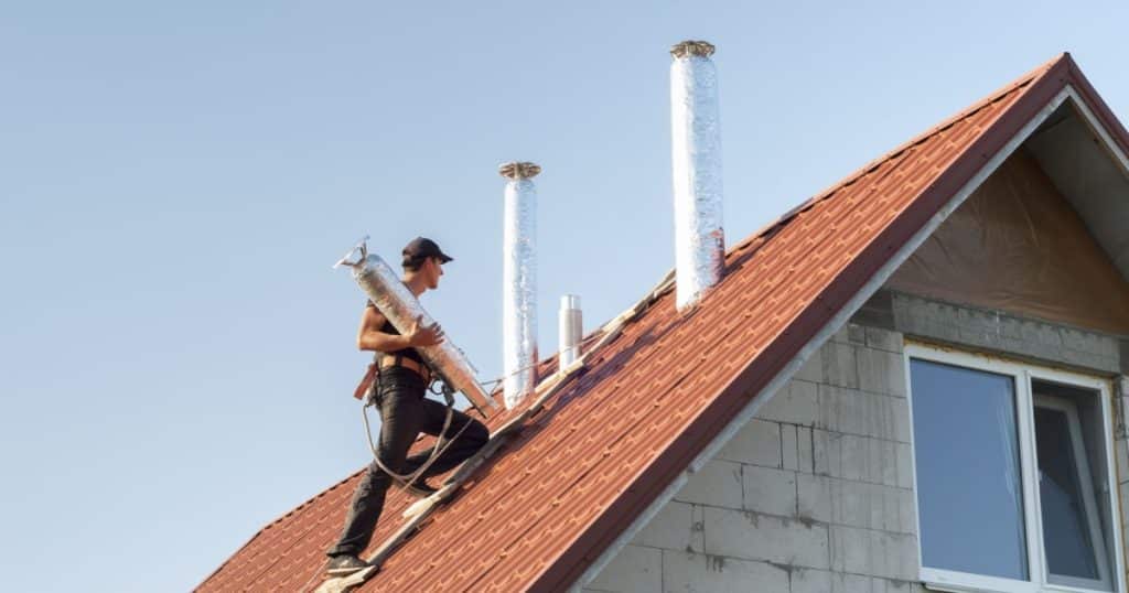 Ouvrier qui monte le conduit de cheminée sur un toit en pente. 