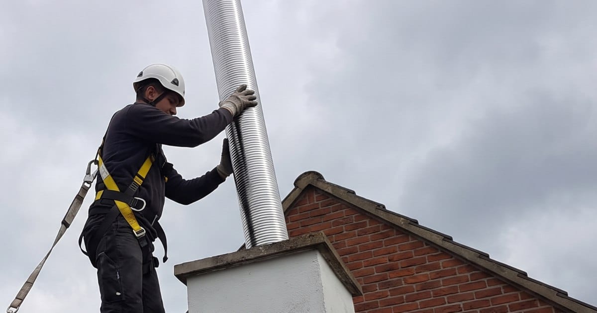 Un ouvrier tubant la cheminée d'un client sur le toit d'une maison en Belgique.
