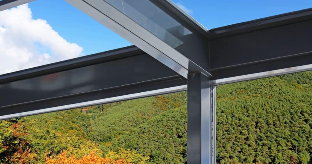 veranda vitrée en aluminium offrant une vue sur une forêt et un ciel bleu
