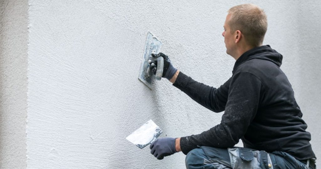 Ervaren gevelwerker in werkkledij brengt witte crepi met geschikt gereedschap professioneel op de buitenmuur aan 