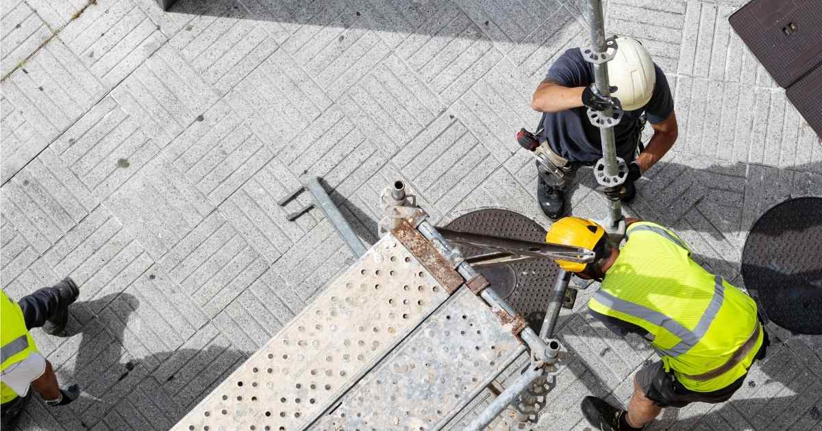 Drie dakwerkers plaatsen een steiger op een betegelde ondergrond voor de renovatie van een plat dak.