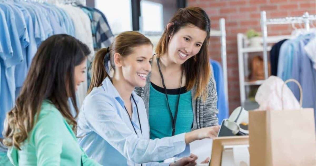 Drie werknemers in een kledingwinkel staan samen achter de kassa.