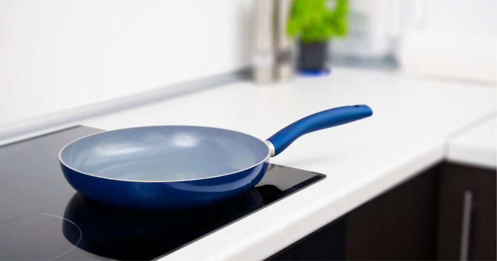 Een blauwe steelpan op een inductiekookplaat in een keuken met wit aanrechtblad en zwarte keukenkasten.