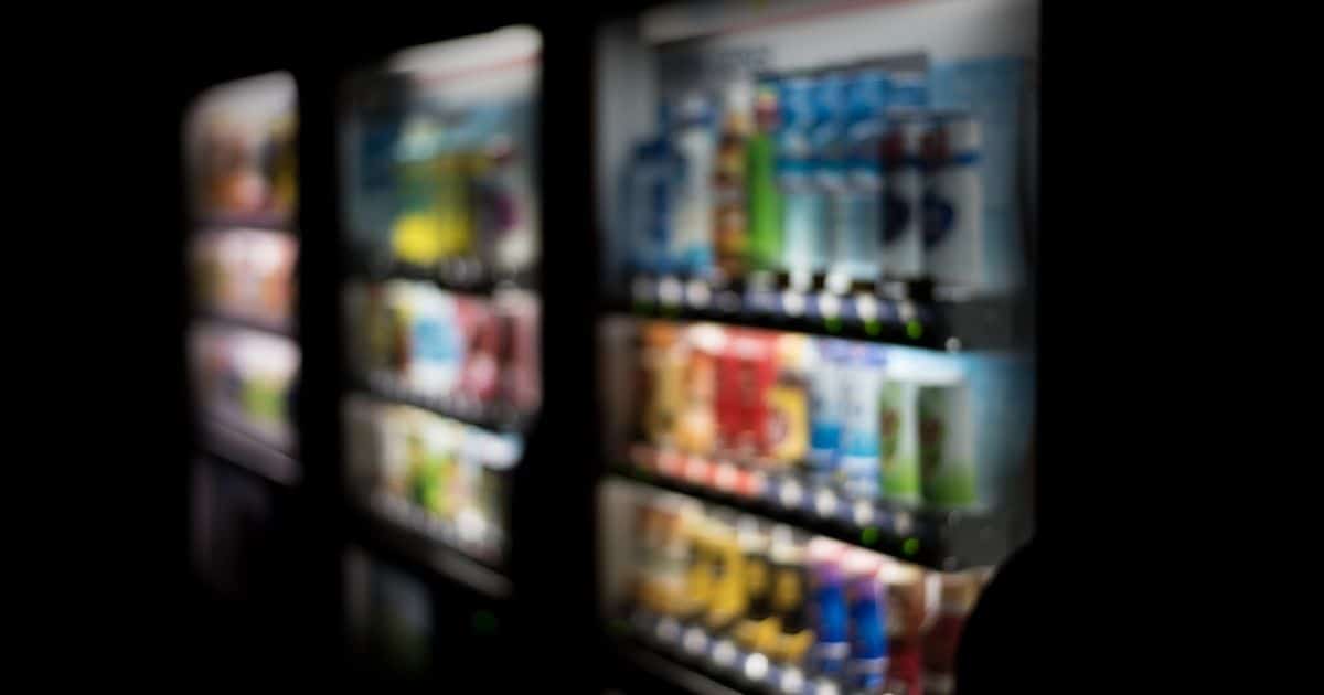 Drie frisdrankautomaten op rij. Het beeld is vervaagd, de achtergrond is zwart. De automaten geven licht waardoor de inhoud deels, maar onscherp, zichtbaar is.