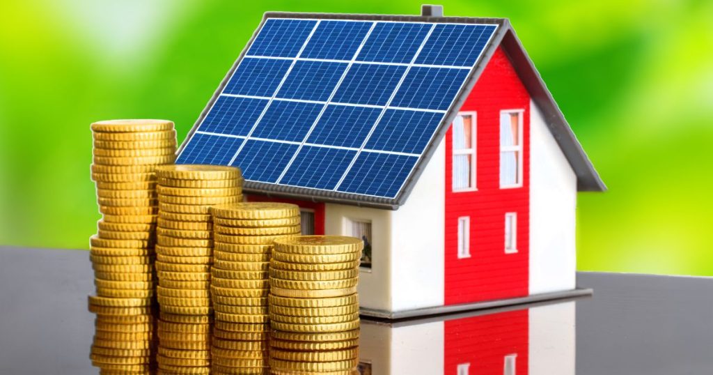 Een klein huisje met zonnepanelen naast stapeltjes met eurocenten op een grijze, reflecterende ondergrond tegen een groene achtergrond.