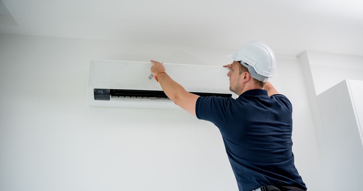 Een professionele airco-installateur met veiligheidshelm bevestigt een airco aan een witte muur.