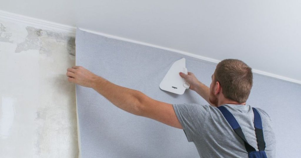 Man die nieuw behang aanbrengt over een vochtige muur 
