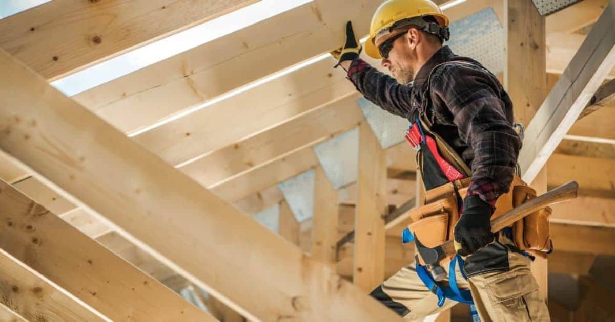 Een dakwerker onder een open, houten dakgebinte tijdens een volledige dakrenovatie.